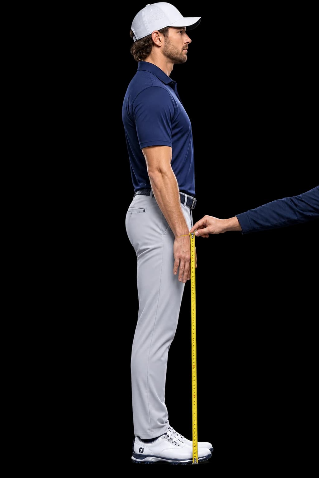 A golfer standing upright with arms relaxed while a helper measures vertically from the wrist crease to the floor